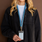 Close-up of a model wearing a blue denim scrunchie lanyard with gold-tone hardware and a clear ID badge holder.