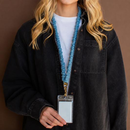 Close-up of a model wearing a blue denim scrunchie lanyard with gold-tone hardware and a clear ID badge holder.