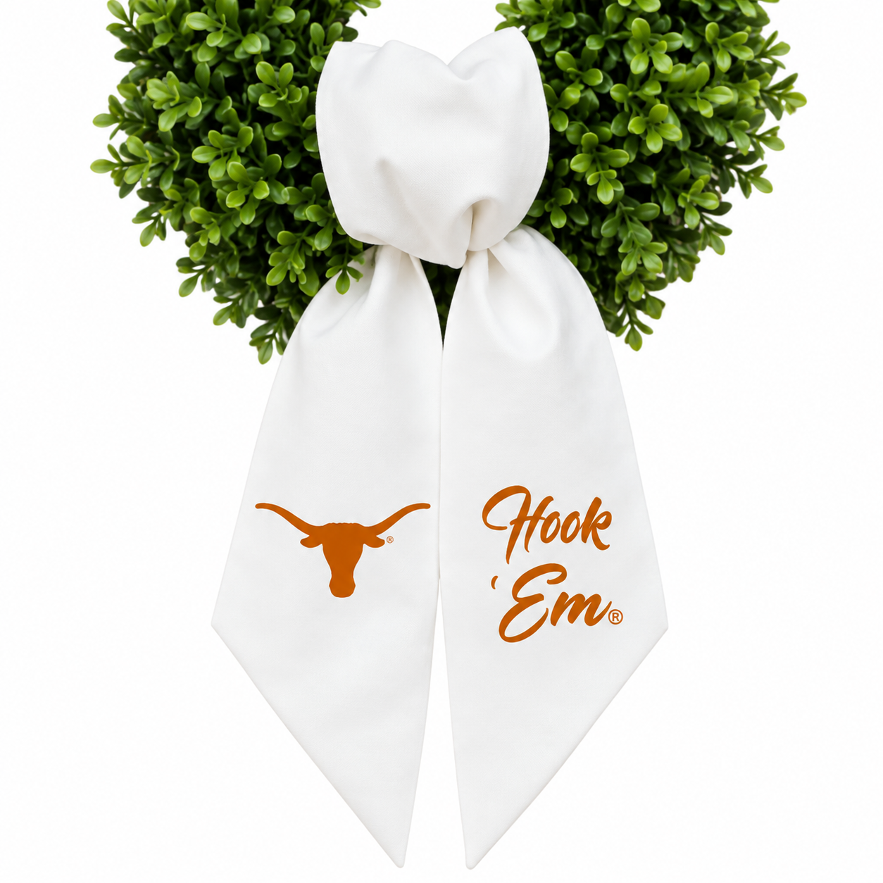 A white bow with orange Texas Longhorns graphics, featuring the Longhorn logo on one side and the words 'Hook 'Em' on the other, tied at the top with green boxwood leaves against a white background.