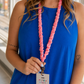 Close-up of a pink pencil-print scrunchie lanyard with antique-brass-tone hardware worn over a blue top.