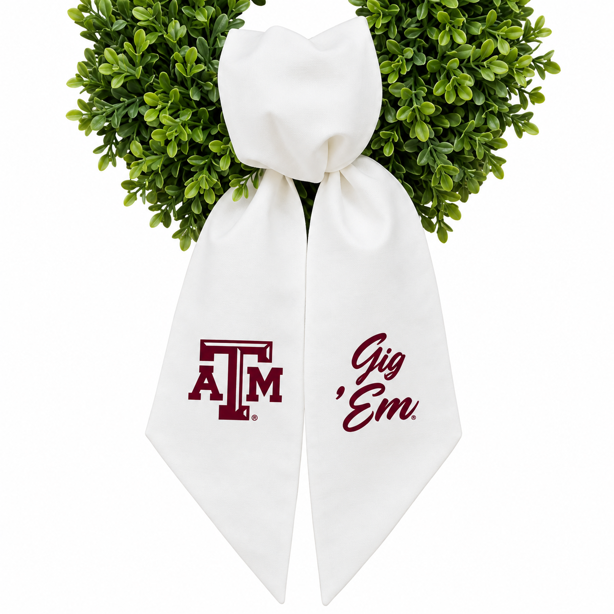A white decorative bow with the Texas A&M 'A&M' logo on one side and the phrase 'Gig 'Em.' on the other, tied with green foliage at the top against a white background.