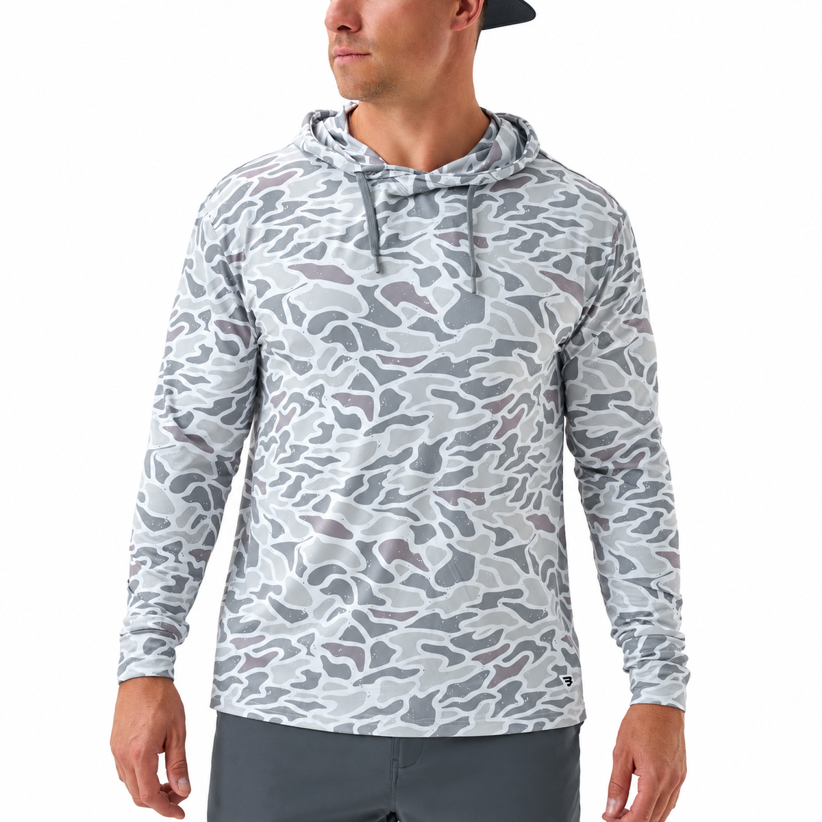 A man wearing a light gray and white camouflage long-sleeve hooded shirt, paired with dark gray pants, against a plain white background.