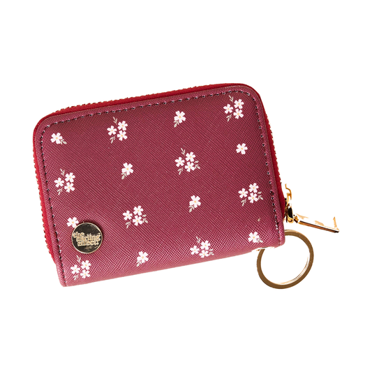 A small zip-around wallet in textured burgundy faux leather with a white cherry blossom pattern, featuring a gold-tone circular logo medallion and a matching gold keyring.